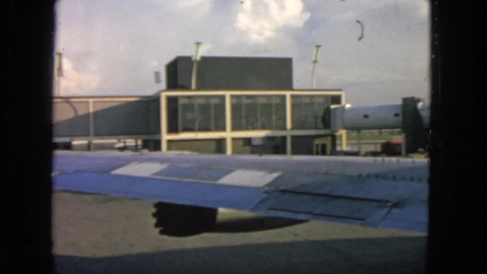 Airplane-window view at San Francisco in 1963, showing the wing, terminal facade, and tarmac structures.