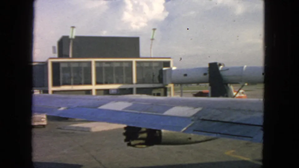 1963 San Francisco airport view from an airplane window, with wing, engine, terminal windows, and jet bridge on the tarmac.