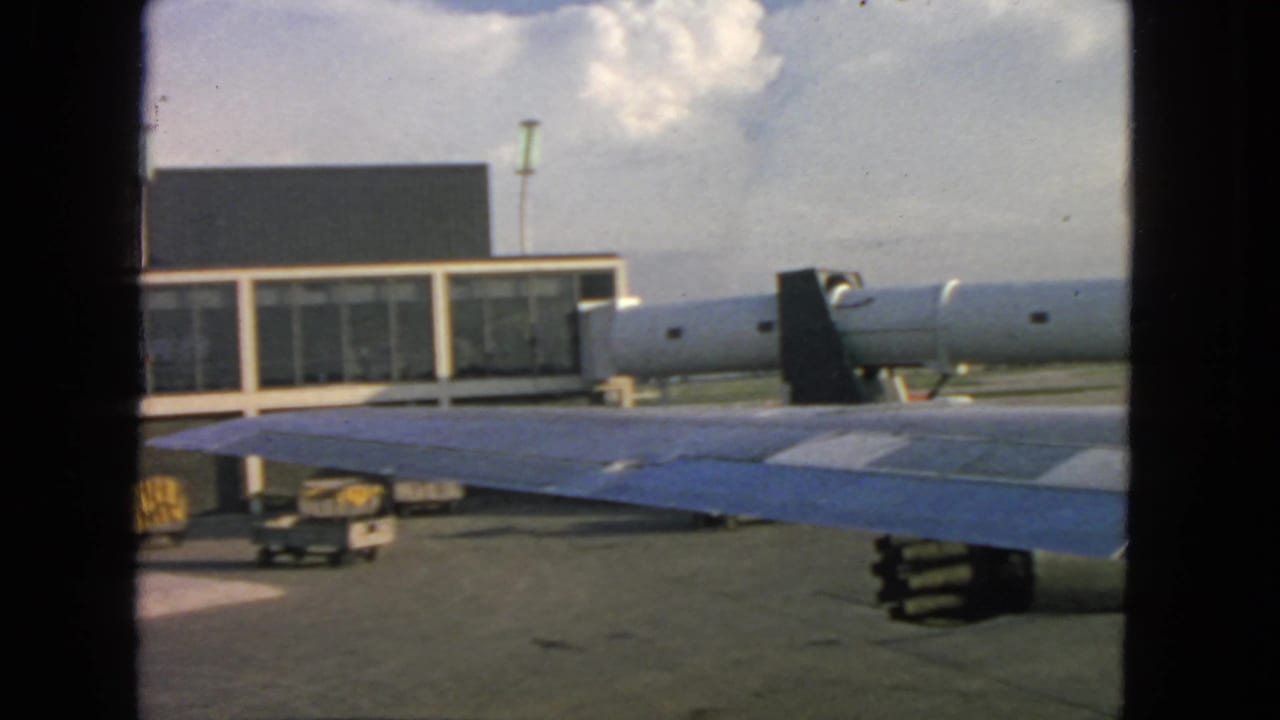 Aircraft wing seen from a window beside an airport terminal and baggage carts.