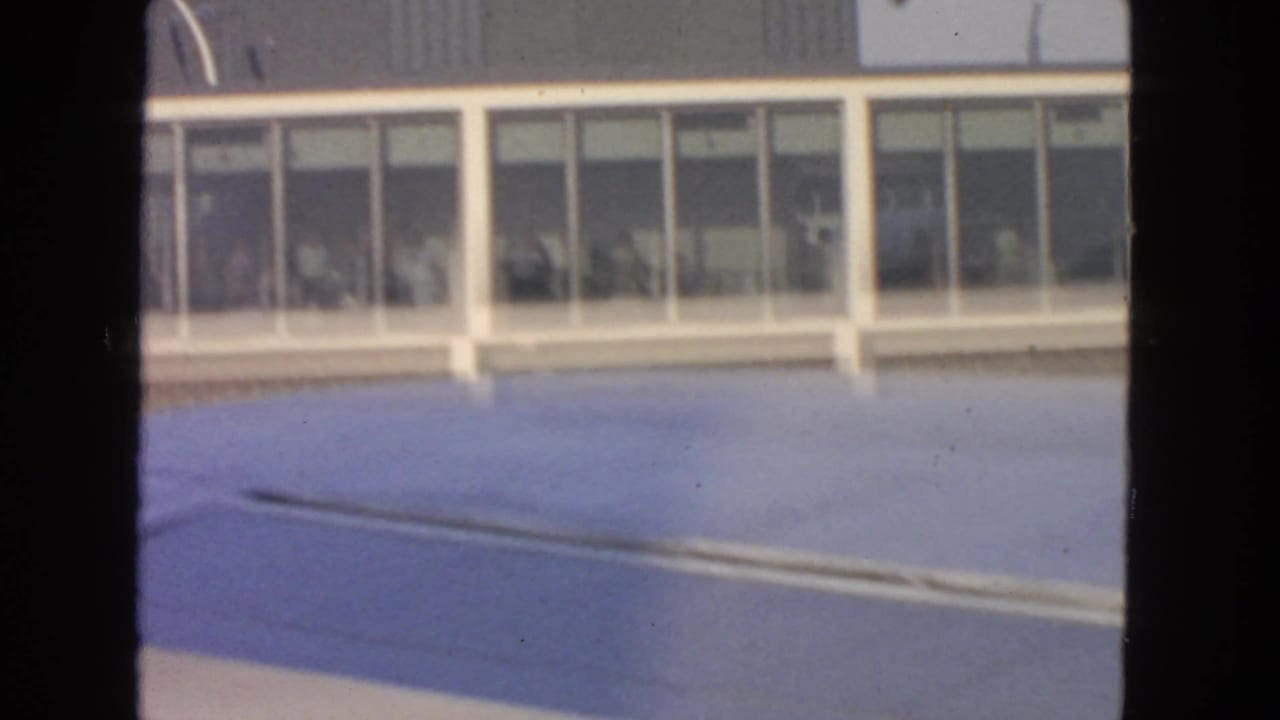 1963 San Francisco airport view with an aircraft wing foreground and passengers visible behind large terminal windows.