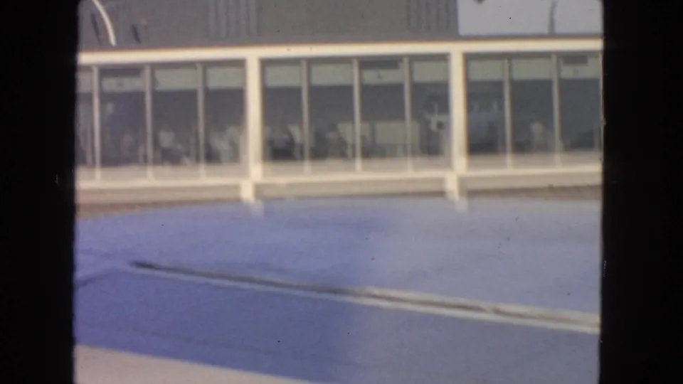 1963 San Francisco airport view with an aircraft wing foreground and passengers visible behind large terminal windows.