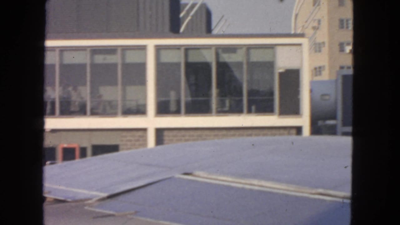 Airport terminal windows seen past an airplane wing or cabin structure, with black film borders.