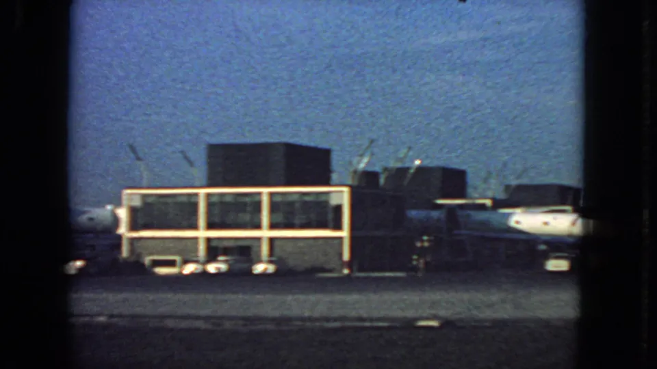 1963 airplane-window view at San Francisco airport, centering a terminal building with parked aircraft and tarmac vehicles.