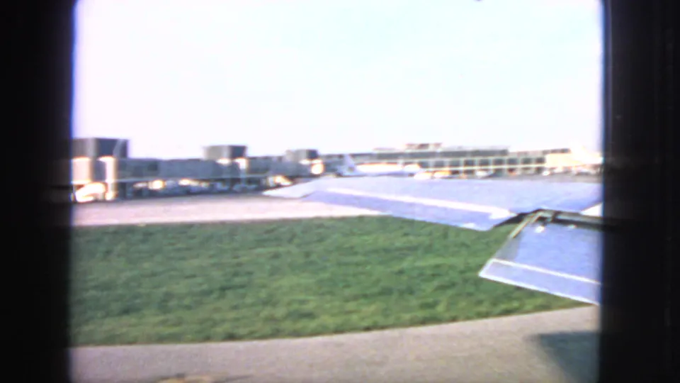 Traveler-style 1963 San Francisco airport view across grass and pavement toward terminal buildings and aircraft wings.