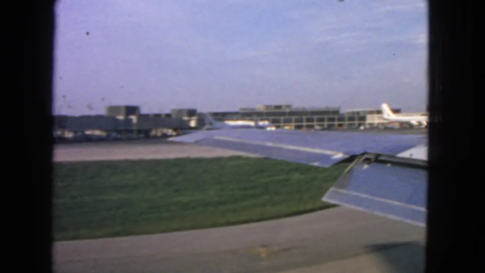 Wide 1963 San Francisco airport view showing grass, pavement, terminal buildings, and parts of aircraft wings.