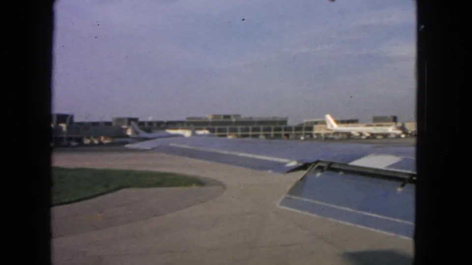 Passenger view at a San Francisco airport in 1963, with the airplane wing in front of terminal gates and parked commercial jets.