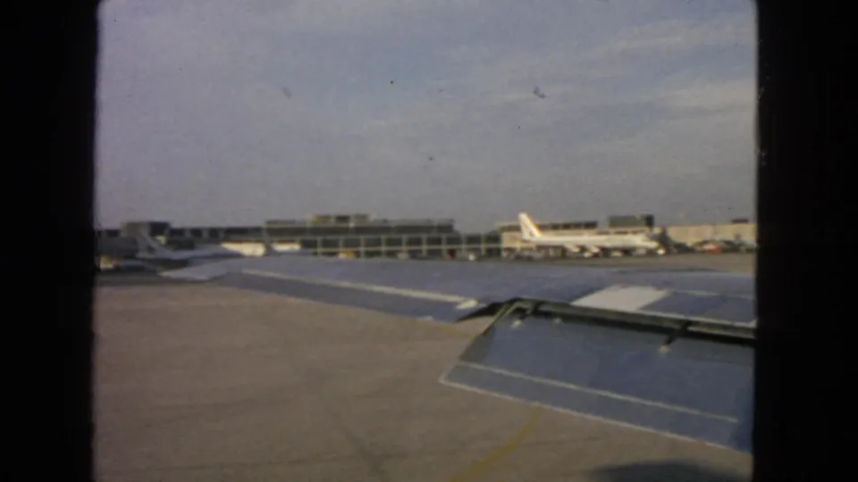 1963 passenger-window footage at a San Francisco airport, showing tarmac, wing surfaces, terminal buildings, and aircraft at gates.