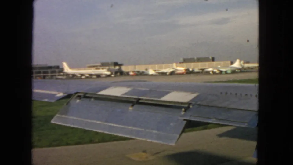Passenger-window view from a taxiing aircraft at San Francisco airport, with wing flap, grass, apron, and distant aircraft visible.