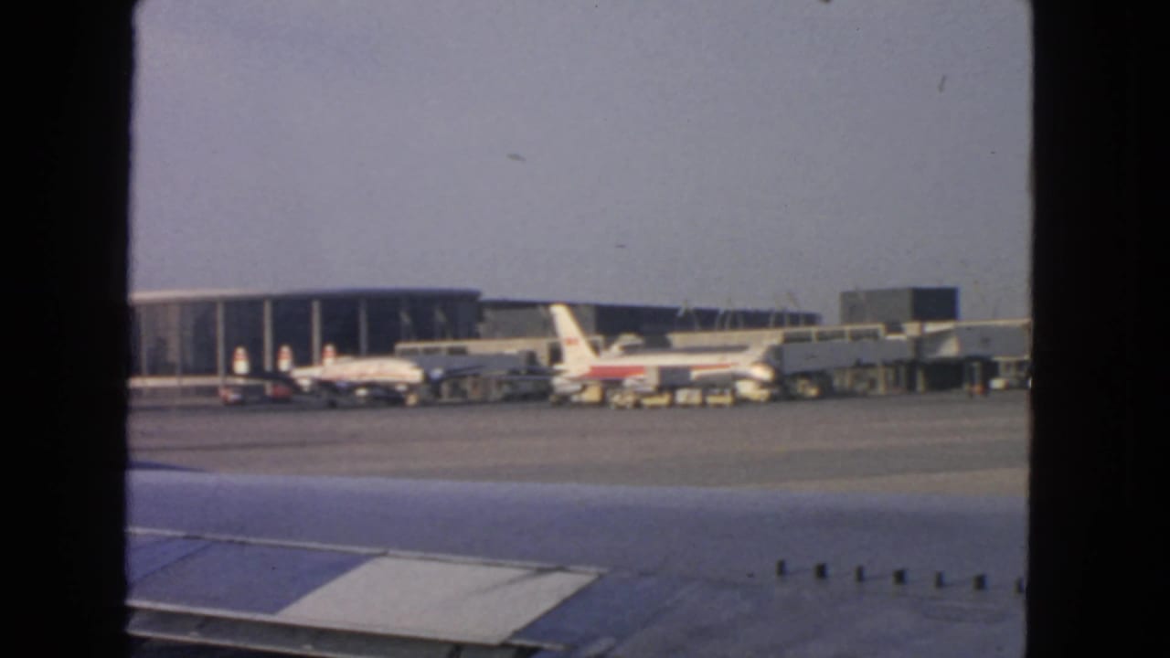 Airport terminal and parked airliners in San Francisco, filmed from inside an aircraft with the wing filling the lower foreground.