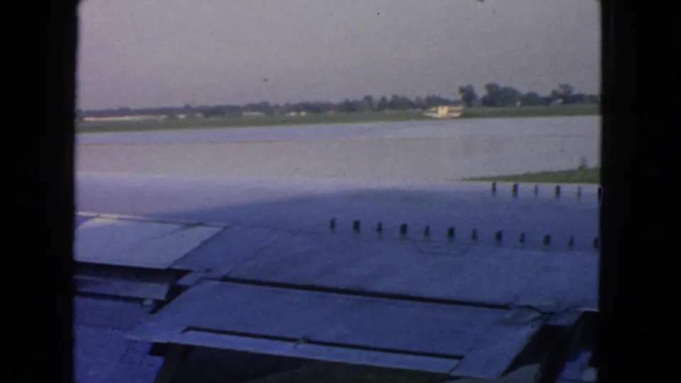 Passenger-window view from the aircraft wing toward airport pavement, water, and distant shoreline in the San Francisco airport area.