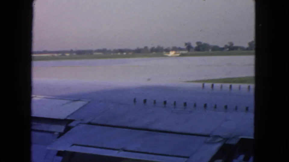 Passenger-window view in the San Francisco area showing the aircraft wing, possible water beside the runway, and distant low structures.