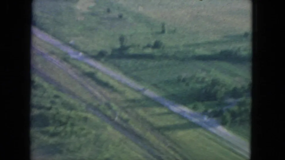 1963 8mm aerial travel view showing rural fields and a diagonal road or track from an airplane window.