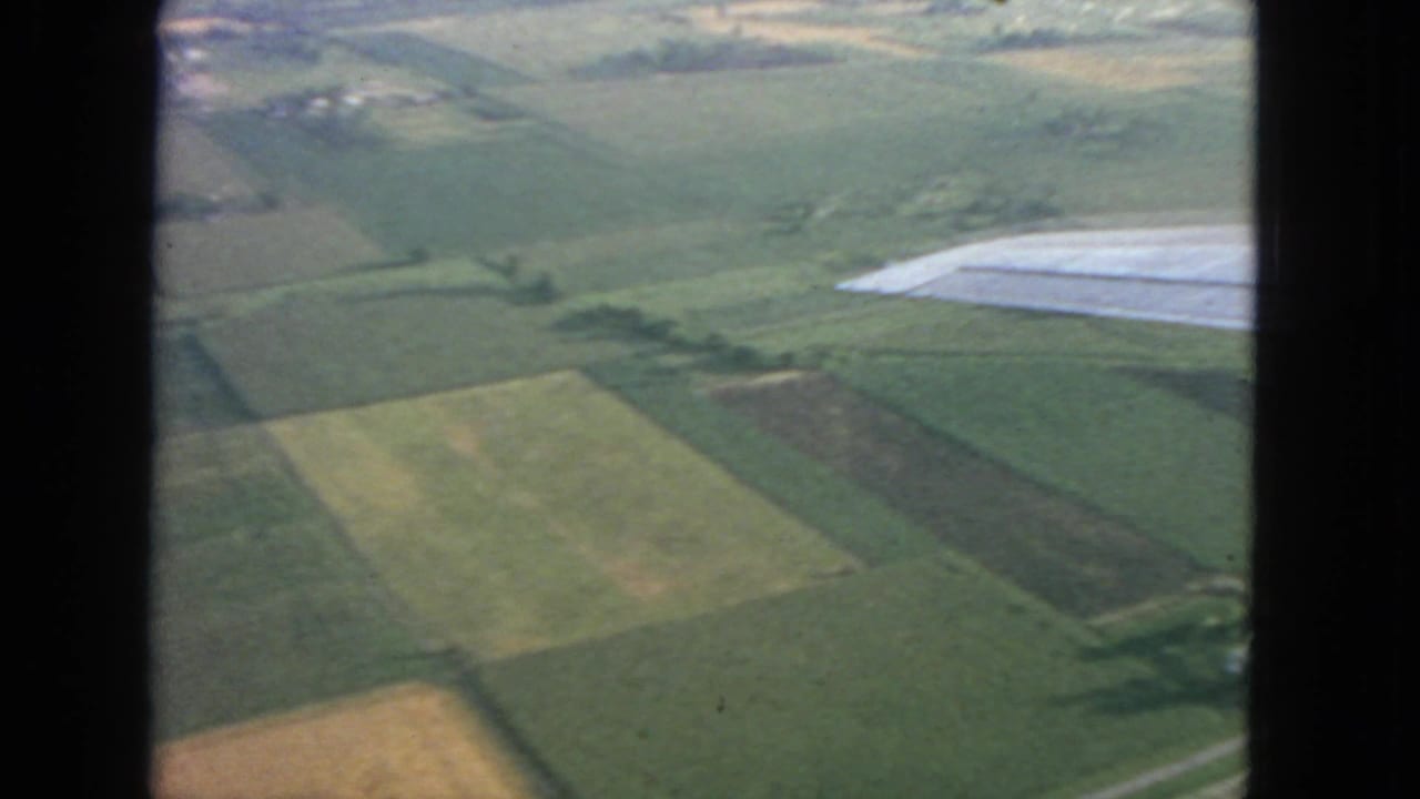 Aerial view of rectangular green and brown fields seen from an airplane window.
