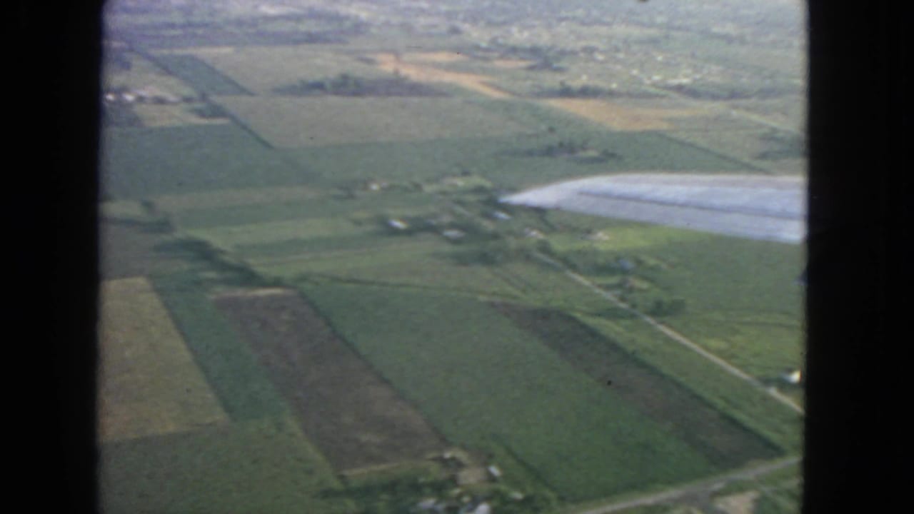 Airplane wing crosses an aerial view of farm fields and rural roads.
