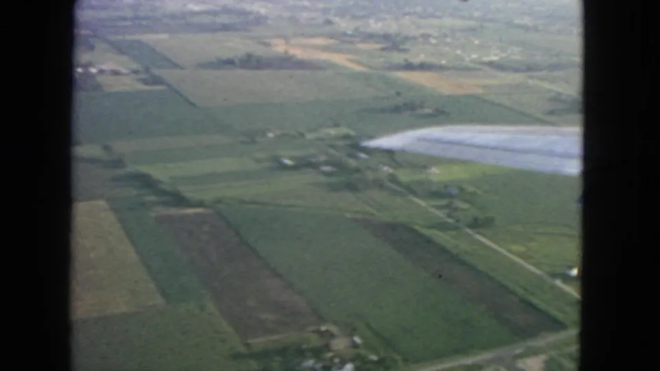 A passenger view from a 1963 flight shows the airplane wing over fields, roads, and scattered rural buildings.