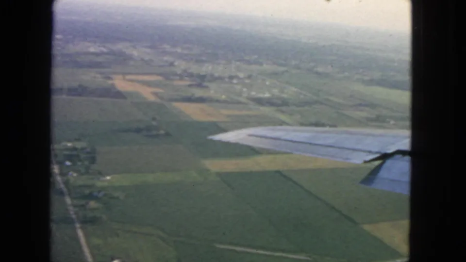 The final 1963 aerial frame looks past the airplane wing toward farmland and a distant built-up area under haze.