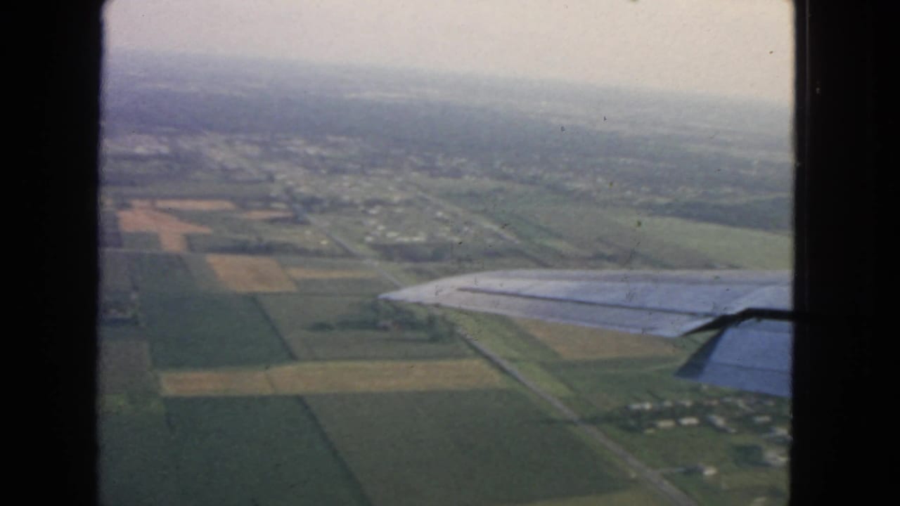 Plane wing at right above farmland, roads, and a small cluster of houses.