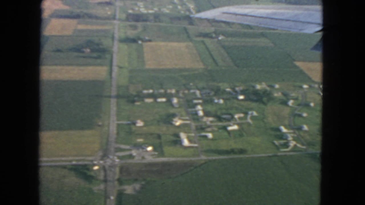 Aerial view of farmland and scattered rural homes seen past an airplane wing.