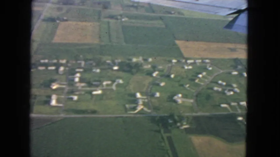 Aerial 1963 home-movie frame showing scattered homes, farmland, and roads below an airplane wing near San Francisco.
