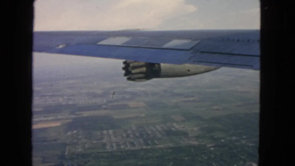 Passenger-window view of a jet wing and engine over suburban land, supported by 1963 San Francisco metadata.