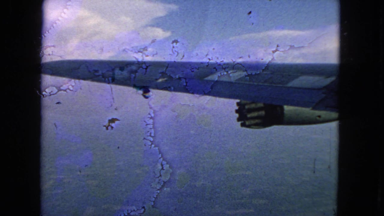 1963 8mm home-movie frame showing an airplane wing and engine from a passenger window, with clouds and water below.