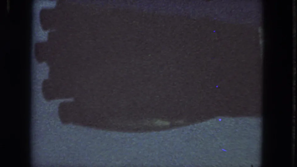 1963 San Francisco 8mm frame showing an indistinct dark shape over a light surface, with sprocket-edge artifacts and aged-film speckling.