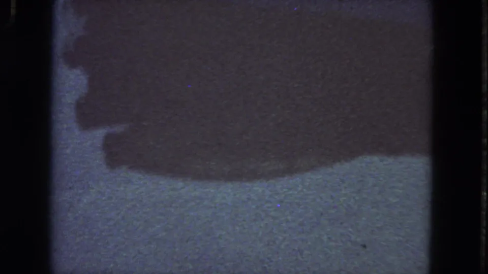 1963 San Francisco 8mm frame with a shadowy process-related object or form, pale surface, visible film edge, dust, scratches, and muted color shift.
