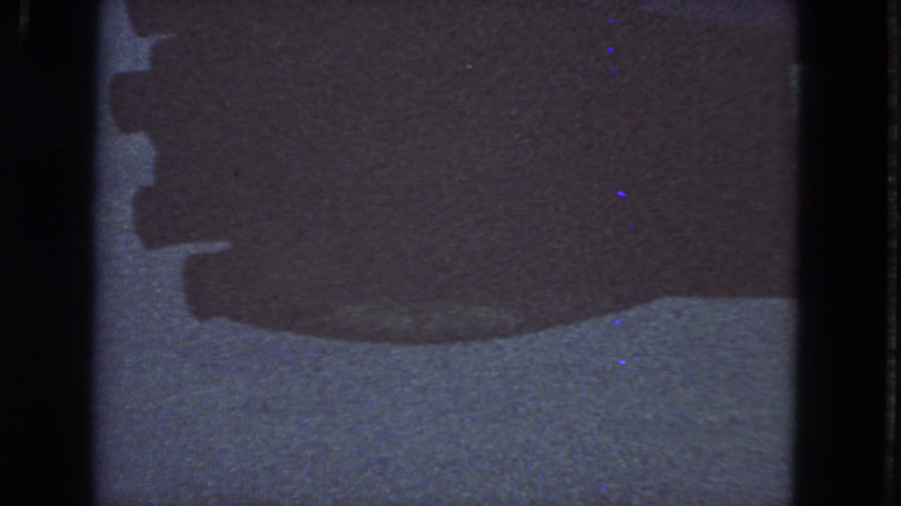 Dark film-framed view with a blue-gray reflective surface and heavy shadow bands.