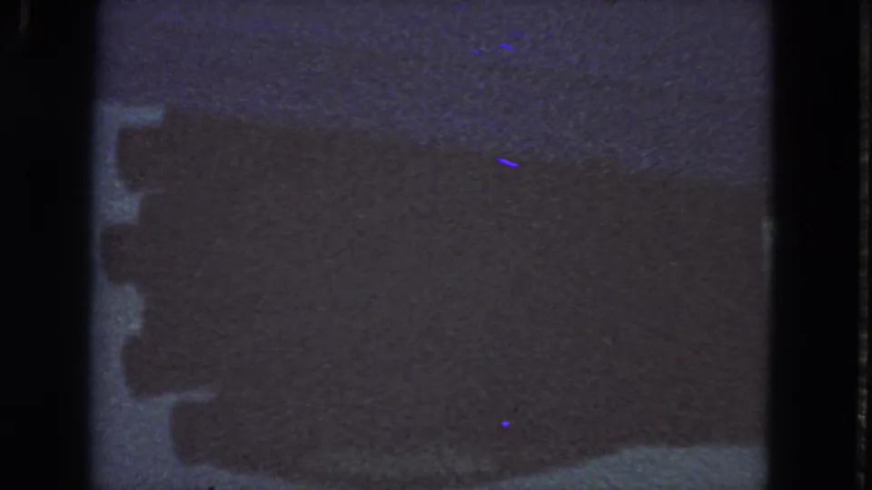 1963 8mm San Francisco frame showing a subdued water or road reflection, dark framing bands, grain, and faint color specks.