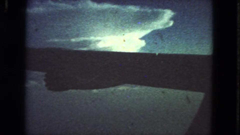 1963 8mm San Francisco frame with bright reflected sky or cloud on a blue-green surface, crossed by dark vehicle or frame shadows.