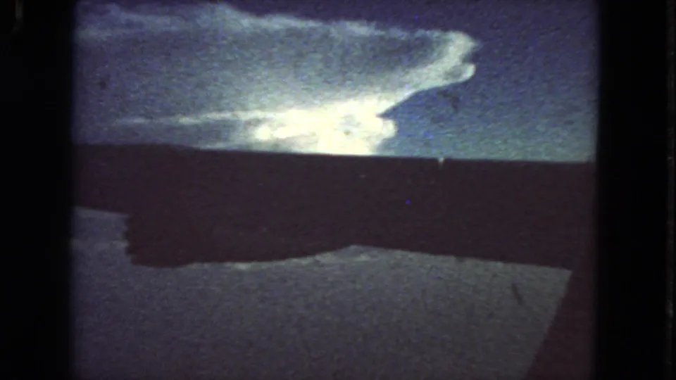 Color 8mm frame shows a luminous cloud formation above a dark horizon, with grain and soft exposure from home-movie film.