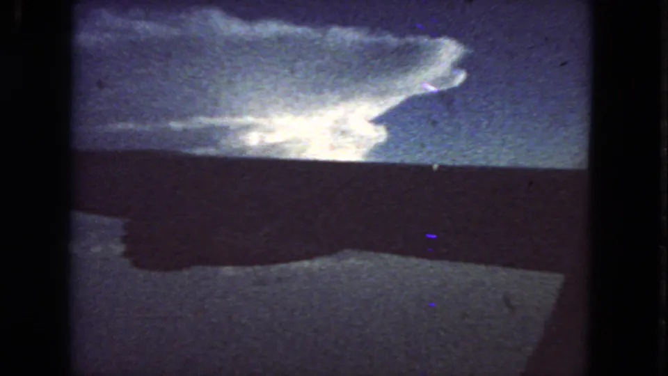 1963 home-movie frame with a large glowing cloud above a dark horizon, seen through soft grain and slight color shift.
