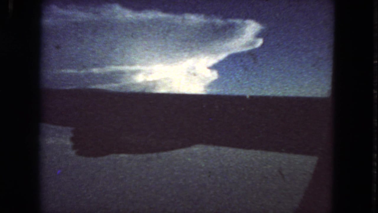 1963 8mm home-movie view from an airplane window, with a dark wing crossing a bright cloudscape above San Francisco-related travel footage.