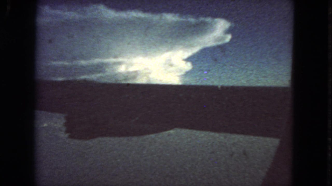 Airplane wing spans the frame with clouds and sky beyond the window.