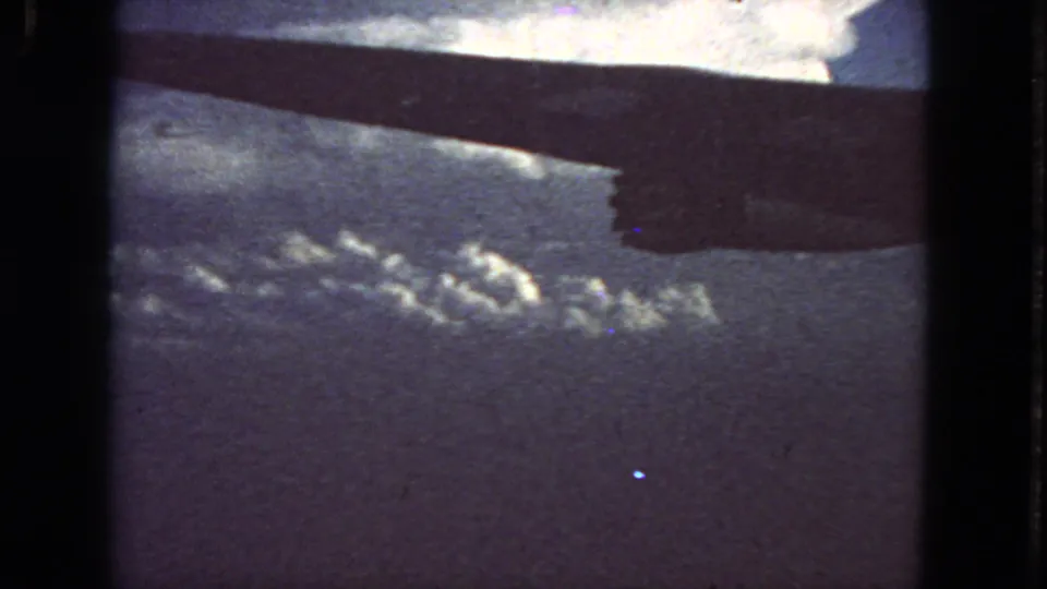 End frame of a 1963 8mm airplane-window view, showing the wing silhouetted above distant clouds with visible film grain.