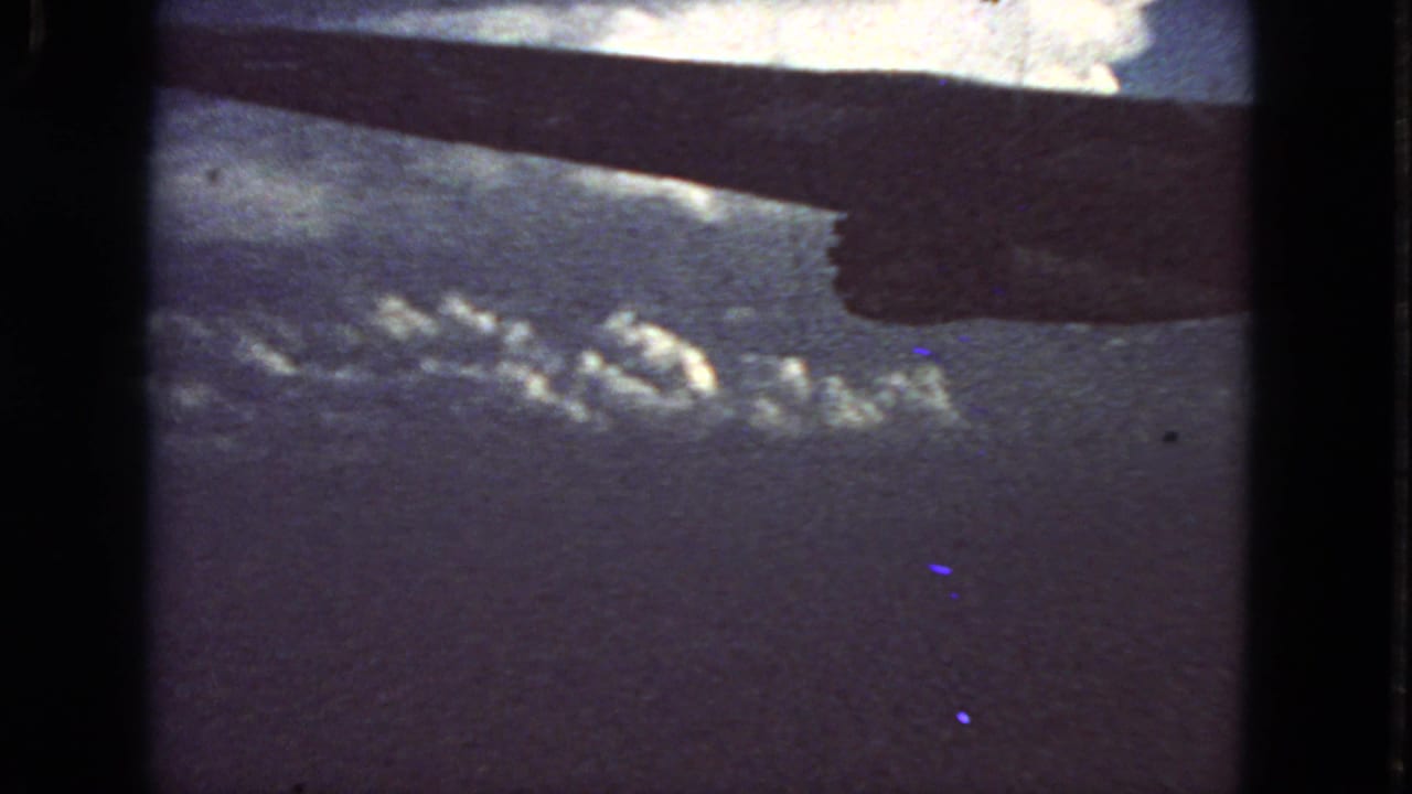 Aircraft wing above a cloud deck seen through a dark 8mm film frame.