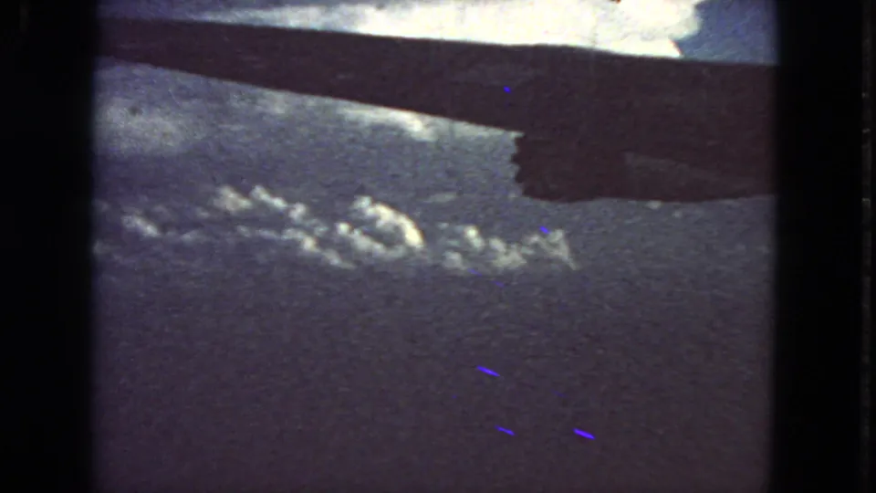 In-flight 1963 8mm view showing the aircraft wing at the top and small cloud formations below.