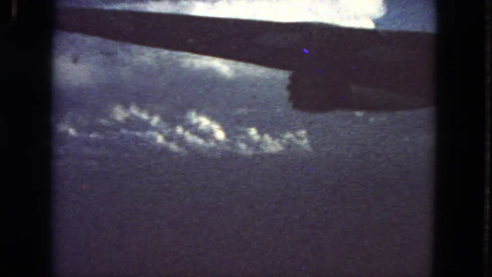 8mm home-movie frame from 1963 showing a passenger-window perspective of wing, sky, and clouds below.