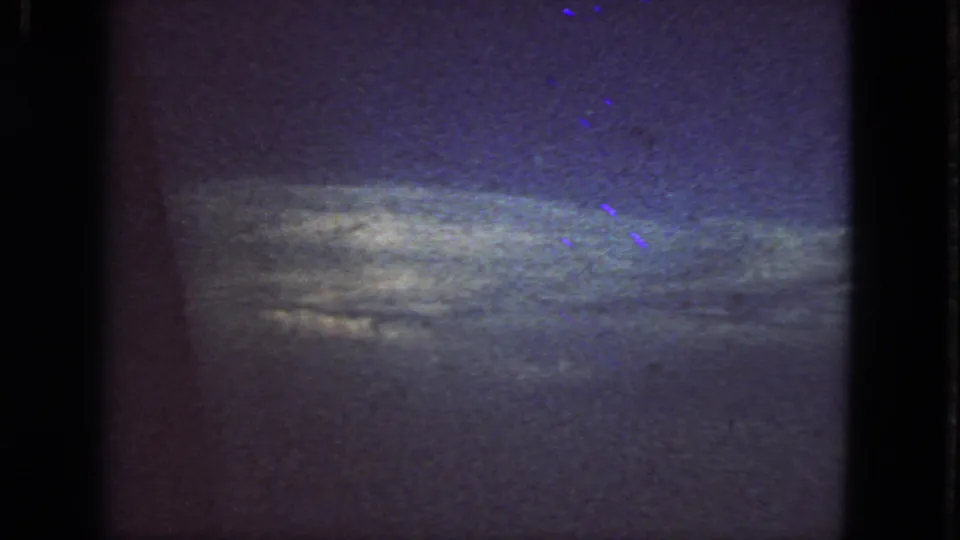 1963 8mm in-flight view with a broad cloud bank and open sky, framed by dark film edges.