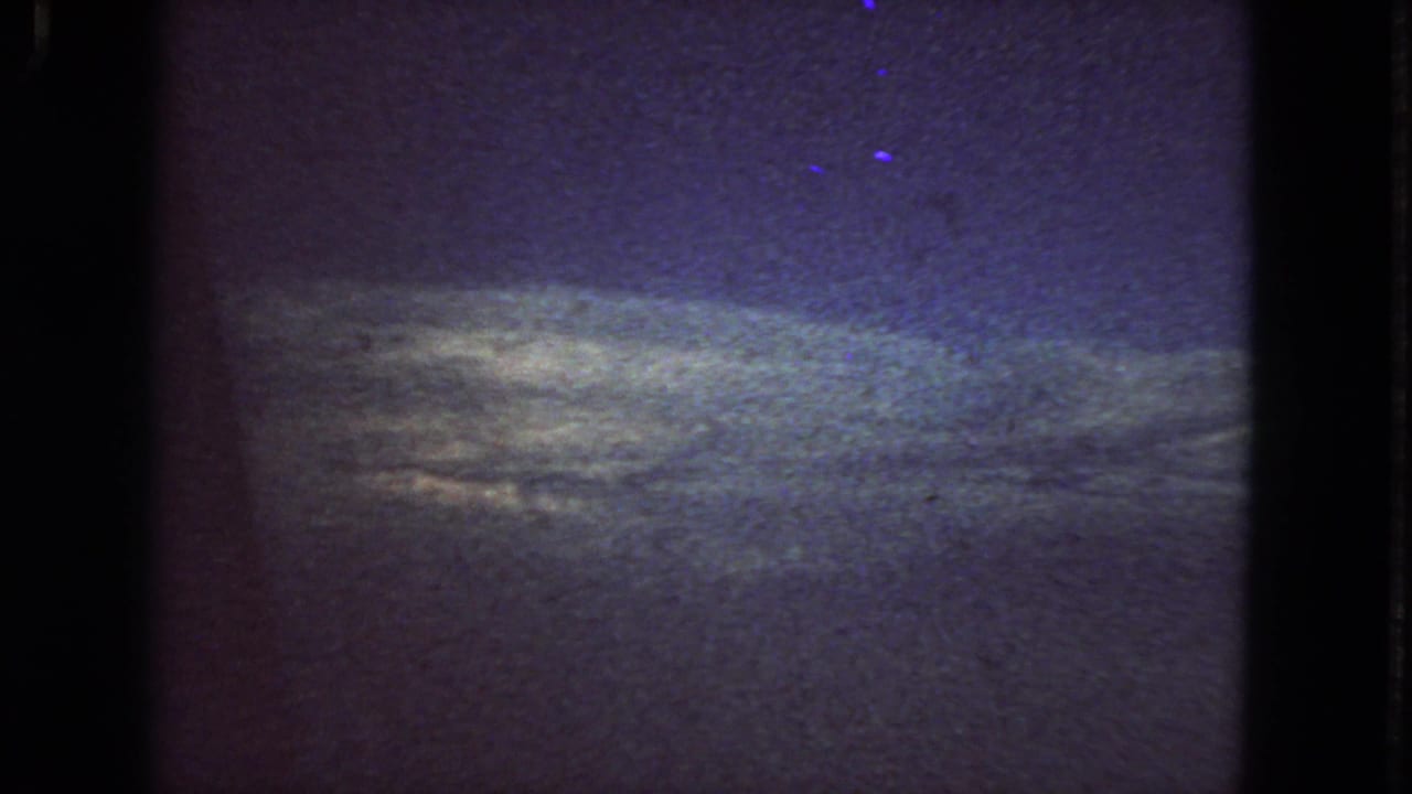 Low-light 1963 San Francisco 8mm frame with a muted horizon glow, dark sky, blue-purple color shift, and pronounced film grain.