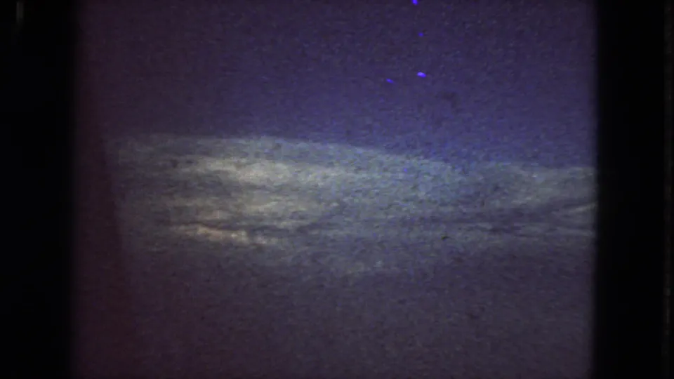 Low-light 1963 San Francisco 8mm frame with a muted horizon glow, dark sky, blue-purple color shift, and pronounced film grain.