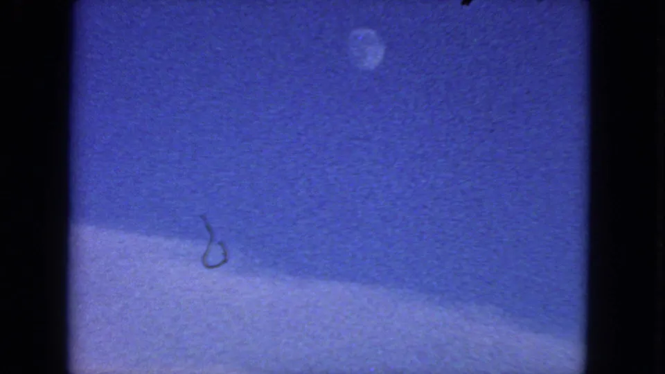 1963 San Francisco 8mm frame showing a small pale moon-like disc in a blue sky above a softly sloping light band and visible dust marks.