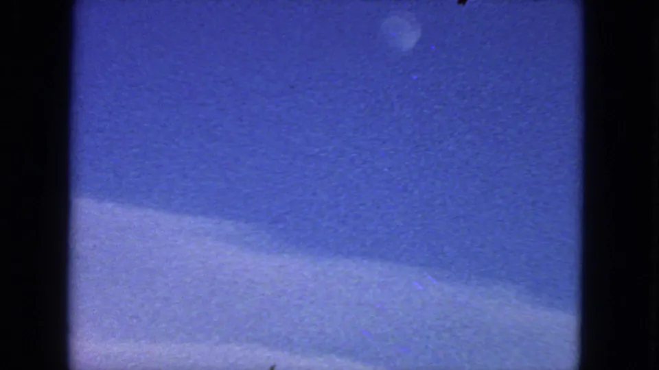 Faded 1963 San Francisco 8mm frame with a faint moon-like disc, blue low-light sky, curved pale lower field, and analog film texture.