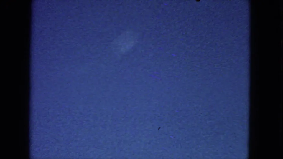 1963 8mm frame with mostly open blue sky, a faint pale cloud boundary, grain, and dark vertical film borders.
