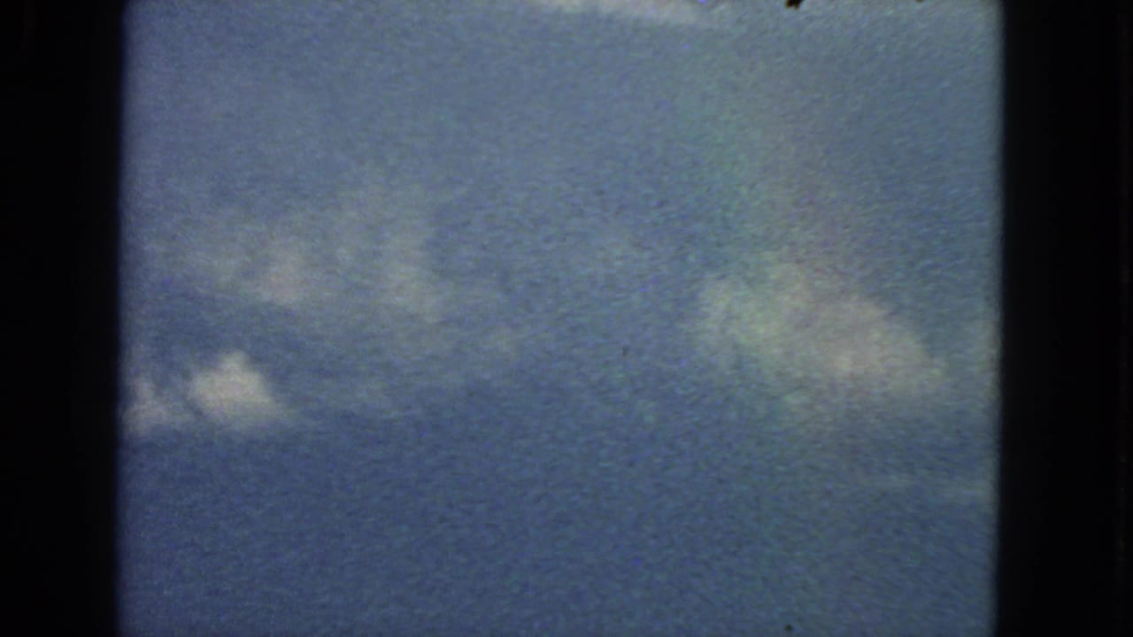 Pale blue sky with small white clouds and dark film gate edges.