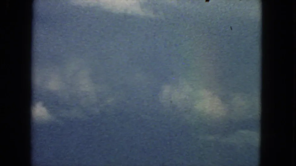 1963 8mm San Francisco sky frame with soft clouds, visible grain, dark gate edges, and slight color variation.