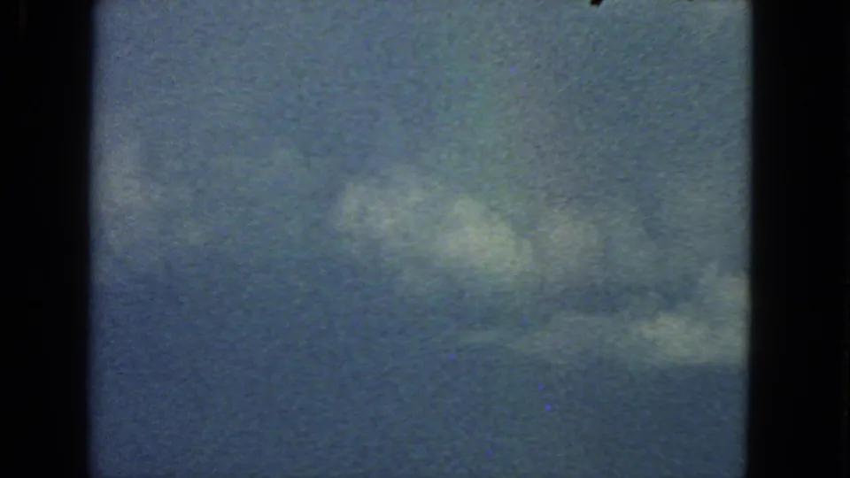 1963 8mm San Francisco home-movie frame showing larger cloud patches, pale blue sky, grain, and visible gate edges.