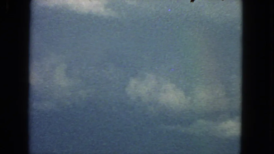 1963 8mm San Francisco sky frame with scattered white clouds, visible grain, dark gate edges, and faint color shift.