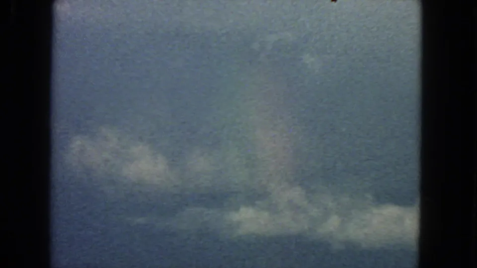1963 San Francisco home-movie frame of a low cloud band across blue sky with dark film borders and soft 8mm grain.