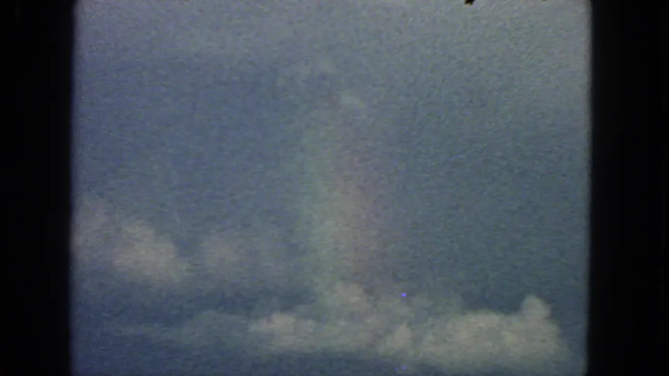 1963 San Francisco 8mm sky view with lower puffy clouds, visible grain, specks, and a subtle rainbow-colored haze.
